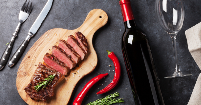 Blog Image Beef & Wine Blog A cutting board with slices of cooked beef set on top of it and a bottle of red wine placed next to it.