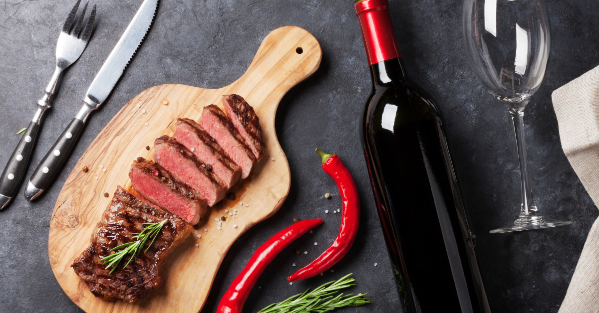 A cutting board with slices of cooked beef set on top of it and a bottle of red wine placed next to it.